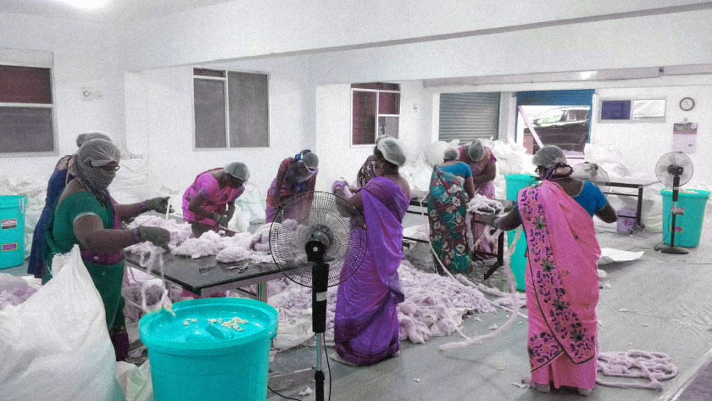 Waste workers — wearing saree, headcaps and face masks — are sorting scraps of textile waste.